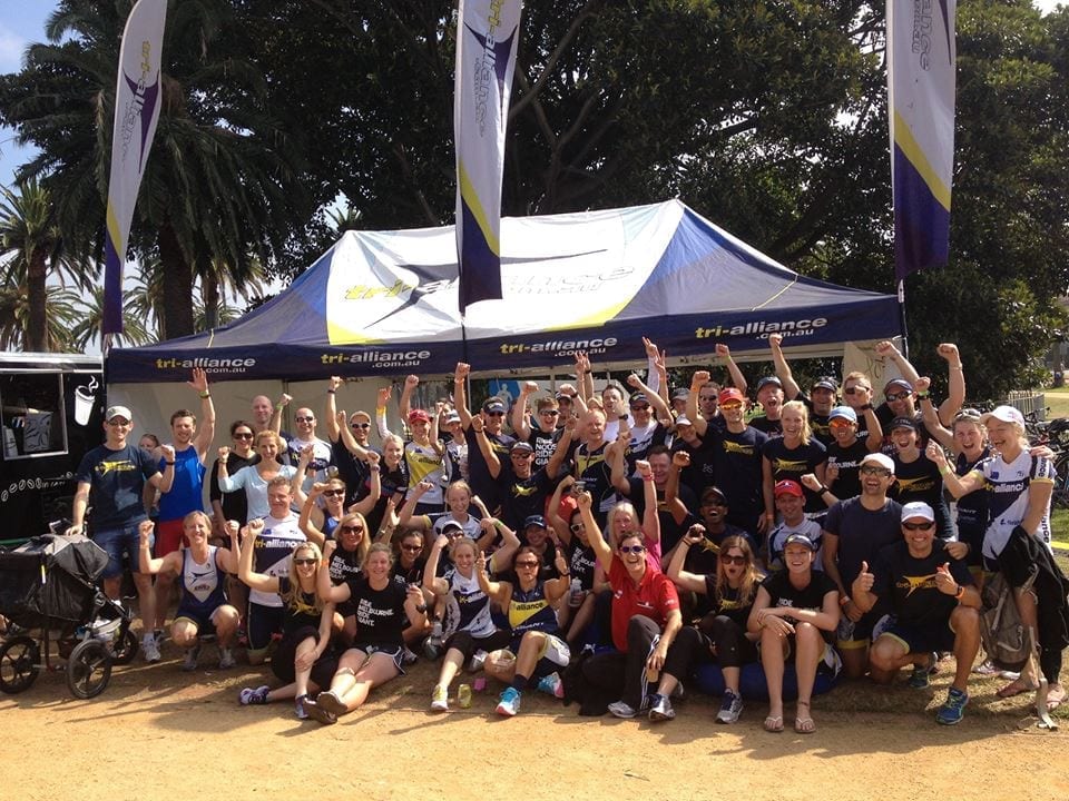 A large Tri Alliance squad gathered together outdoors with arms raised