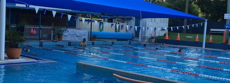 Outdoor swimming pool with swimmers, blue canopy, and lane dividers.