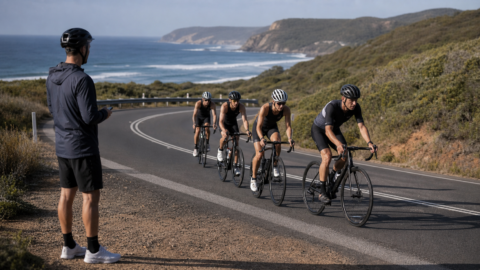 Tri Alliance squad riding steadily in a bunch on an open coastal road during a long training ride, coach watching on