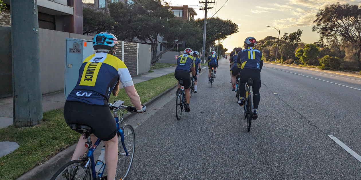 Tri Alliance squad riding together at sunrise, one rider easing off the back of the bunch
