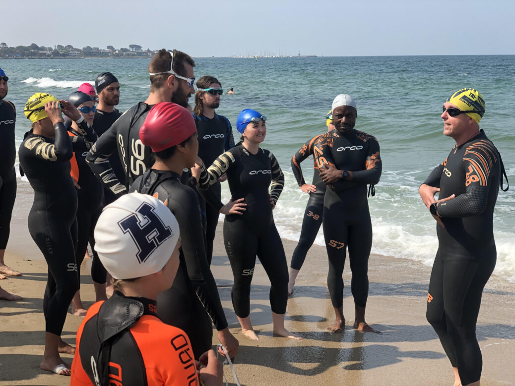 Swimmers in wetsuits standing on a sandy beach near the ocean