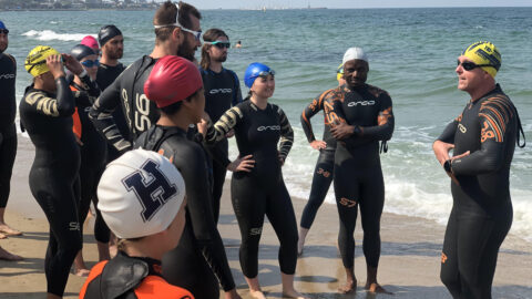 Swimmers in wetsuits standing on a sandy beach near the ocean