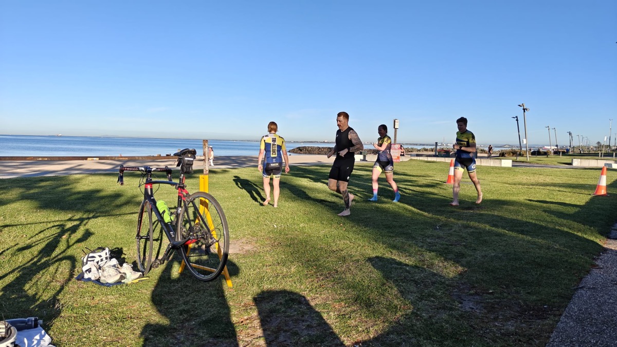 Tri Alliance athletes in team kit heading out on the grass beside Port Phillip Bay at Elwood during a combo session