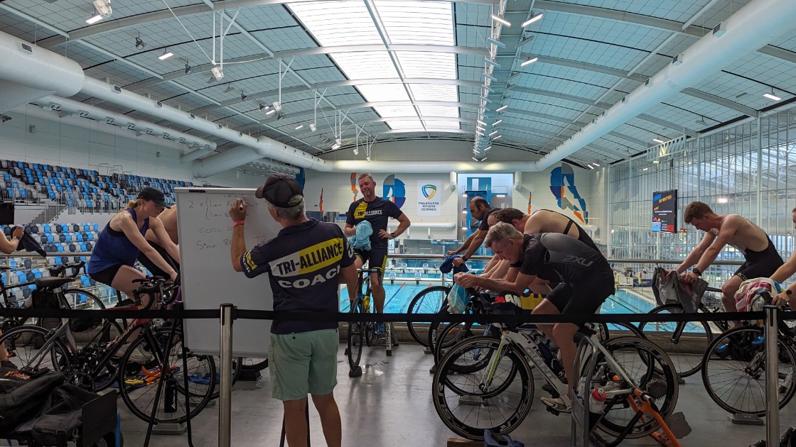 Tri Alliance athletes on wind trainers at MSAC with drink bottles and nutrition within reach during a coached session
