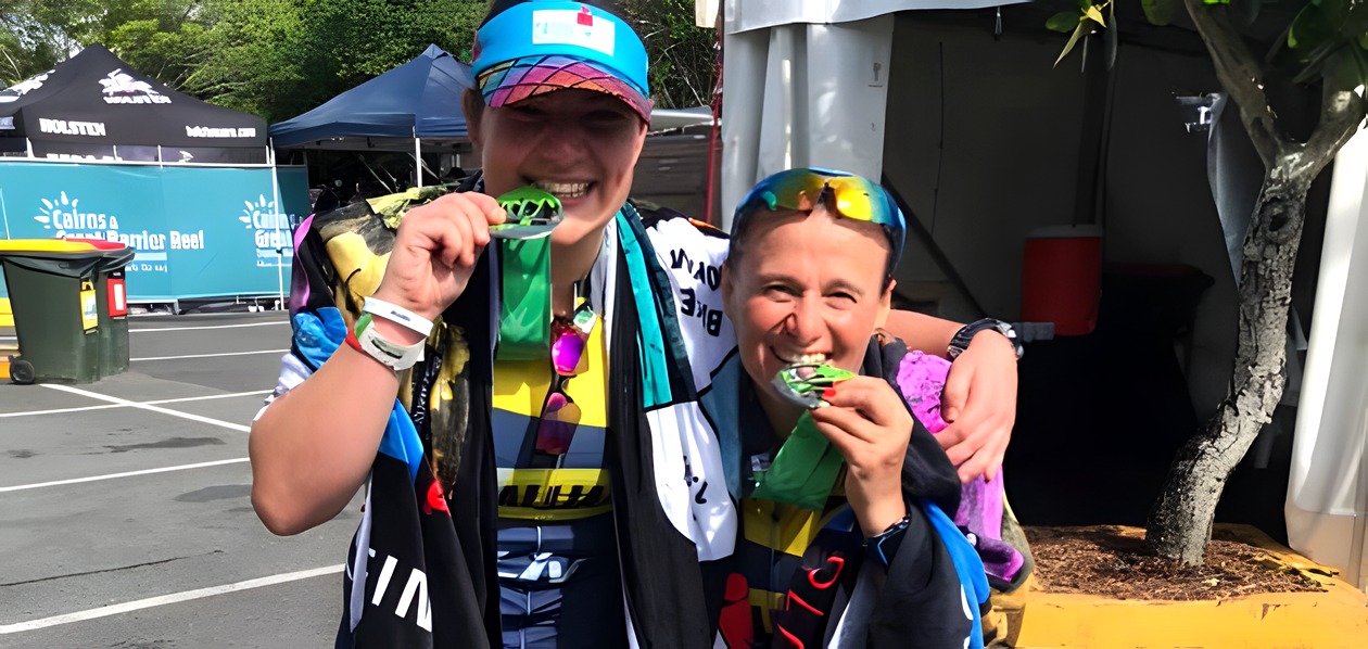 Two Tri Alliance women biting their finisher medals at Ironman 70.3 Cairns