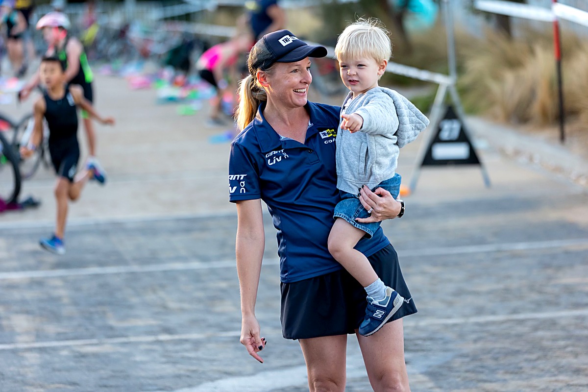 A Tri Alliance coach holding her toddler at a triathlon