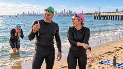 Three triathletes in wetsuits checking the water temperature before an open-water swim